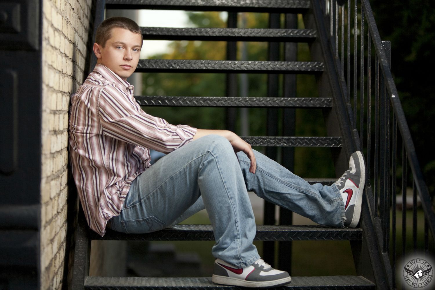 Fashion like senior portraits in Austin, Texas, of young man in pink striped shirt and jeans on a staircase.